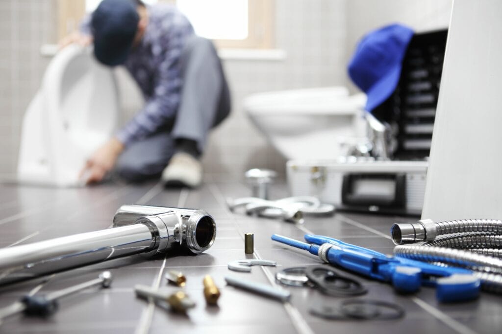 Image of a plumber working on a toilet with tools displayed in the foreground. What Questions Should You Ask Before Hiring a Plumber?