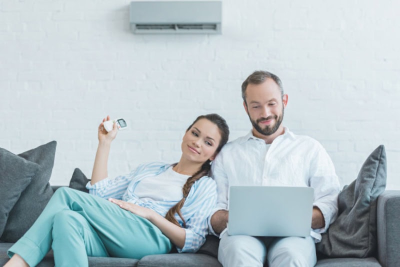 couple sitting on couch, using a remote to adjust their ductless unit.