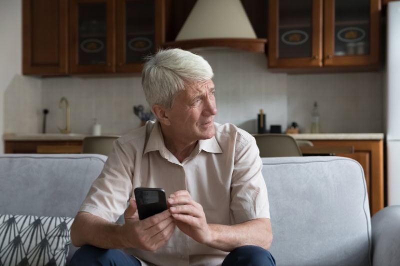 What’s That Smell Coming From My Furnace? Photo of a man on his phone, sitting on the couch and looking outside seemingly concerned.