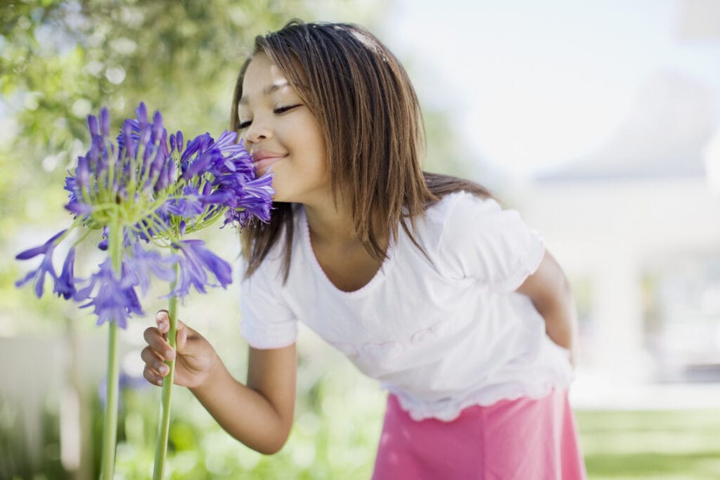 young girl smelling a purple flower outside.