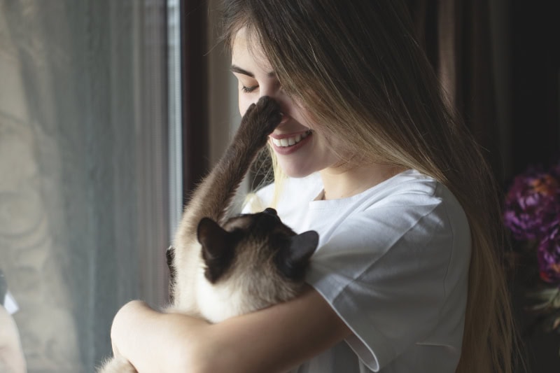 young woman hugging her cat in front of the window.