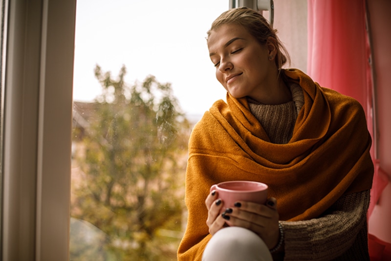 5 Tips to Improve Your Indoor Air Quality This Fall - Woman Sitting by the WIndow.